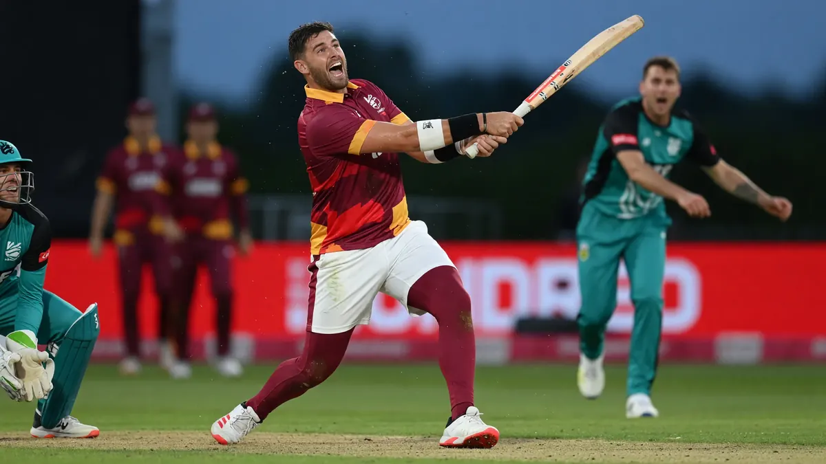 Batter in maroon and yellow kit celebrating a big hit as the teal wicketkeeper and fielder react under lights